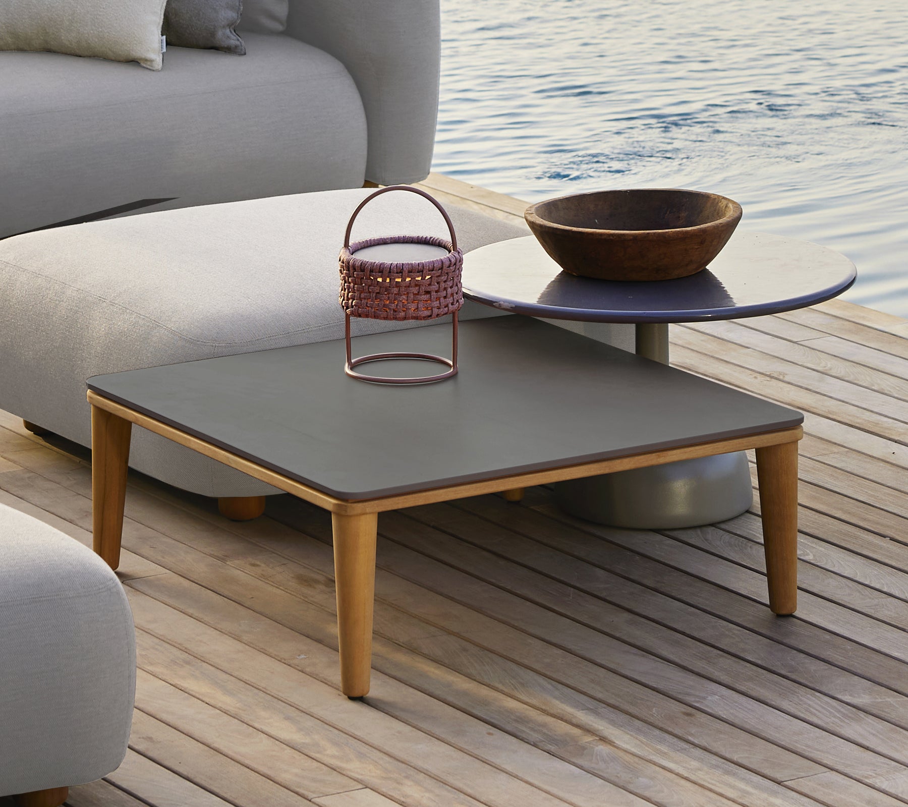 Mesa gris moderna con un cuenco de madera y una cesta de metal en un entorno al aire libre.