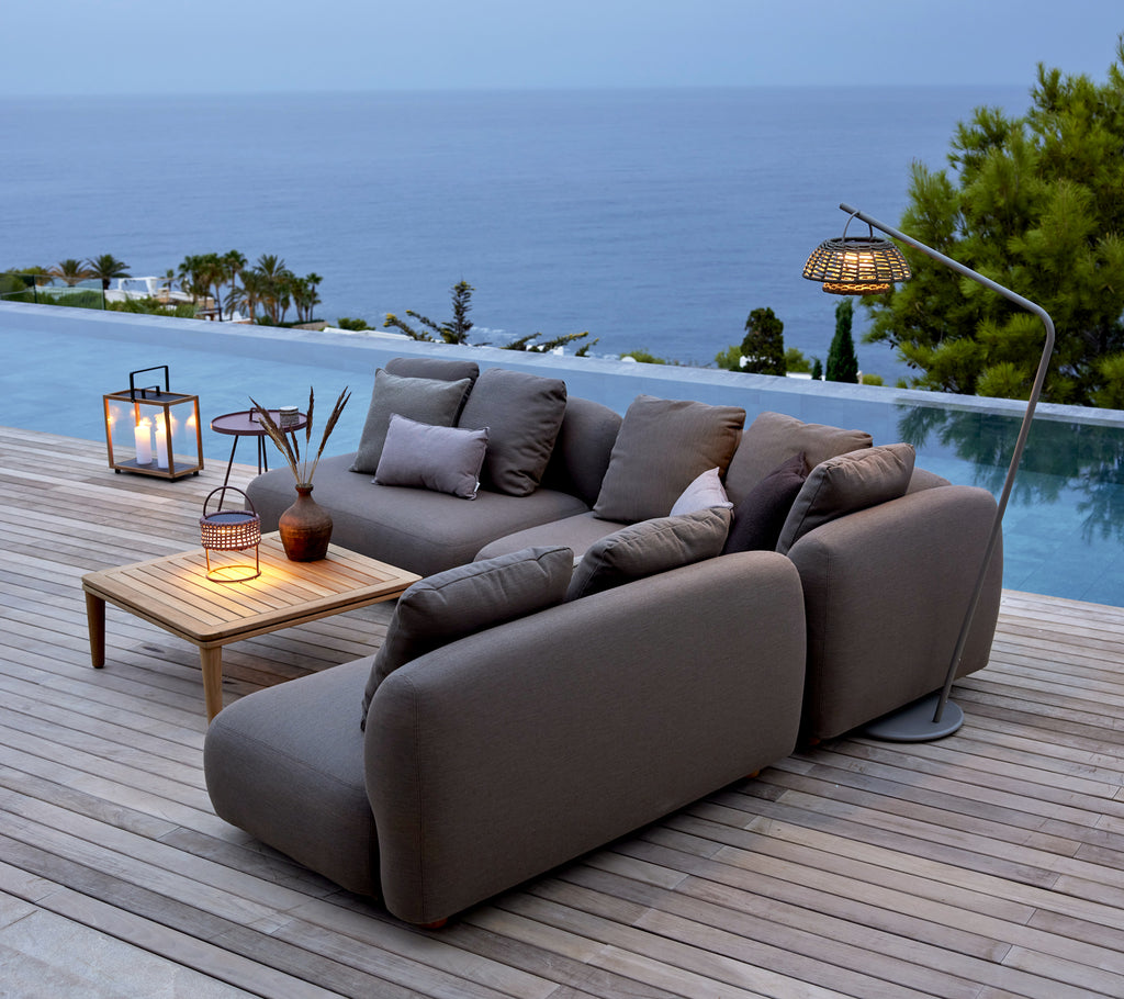 Sofá gris con mesa de madera y faroles junto a una piscina con vista al océano.