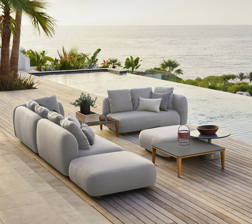 Sofá gris elegante con cojines y una mesa de café negra en una moderna sala de estar al aire libre junto al mar.