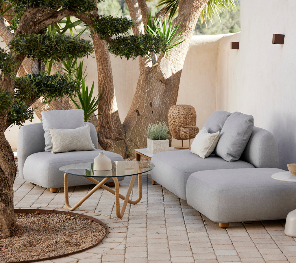 Sofá y silla grises contemporáneos con una mesa de vidrio en una elegante zona de salón al aire libre.