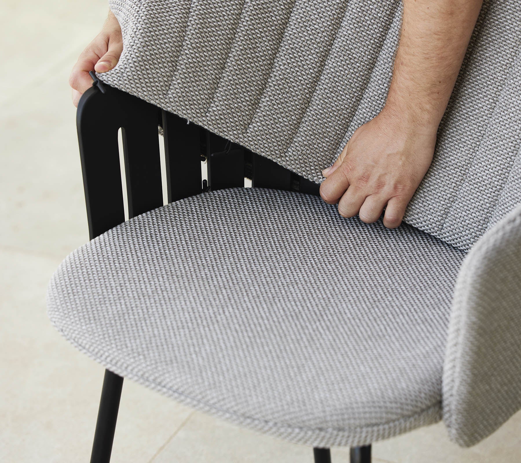 Una persona ajusta el respaldo de una silla moderna con un asiento de tela texturizada, mostrando un diseño elegante y soporte ergonómico.