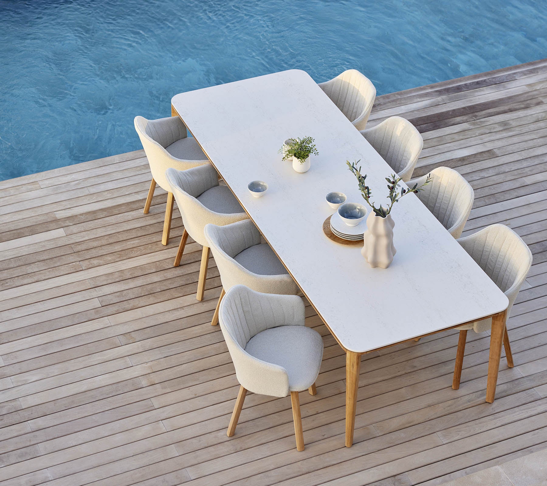 Configuración de comedor elegante con una mesa larga rodeada de cómodas sillas, adornada con un jarrón y acentos de plantas.