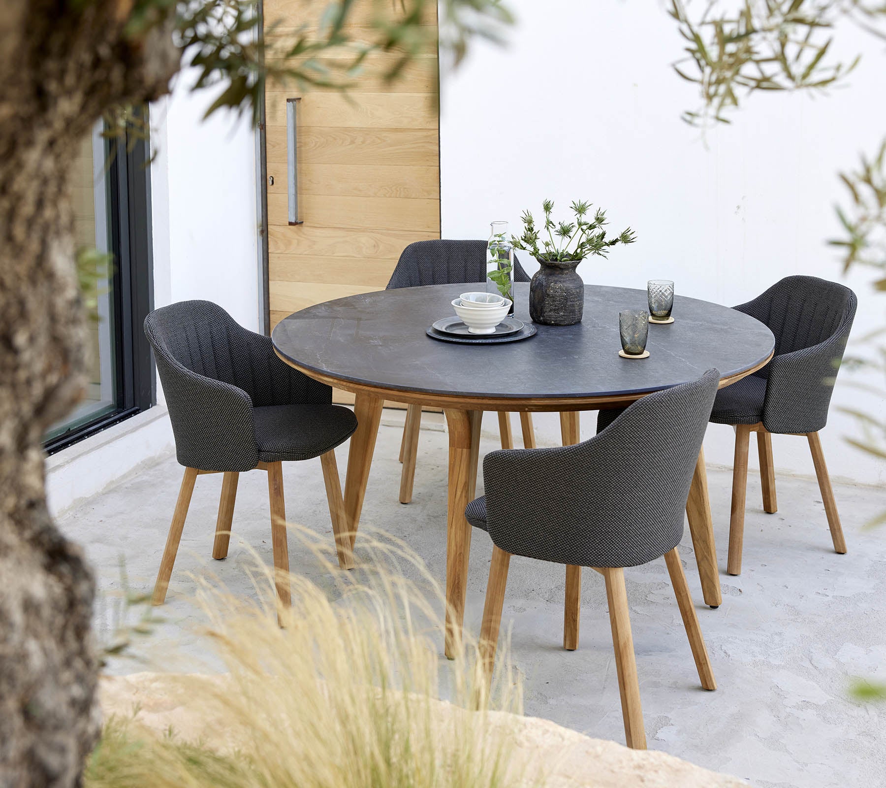 Una mesa redonda rodeada de cuatro sillas elegantes, con un centro de flores y una simple disposición de la mesa.