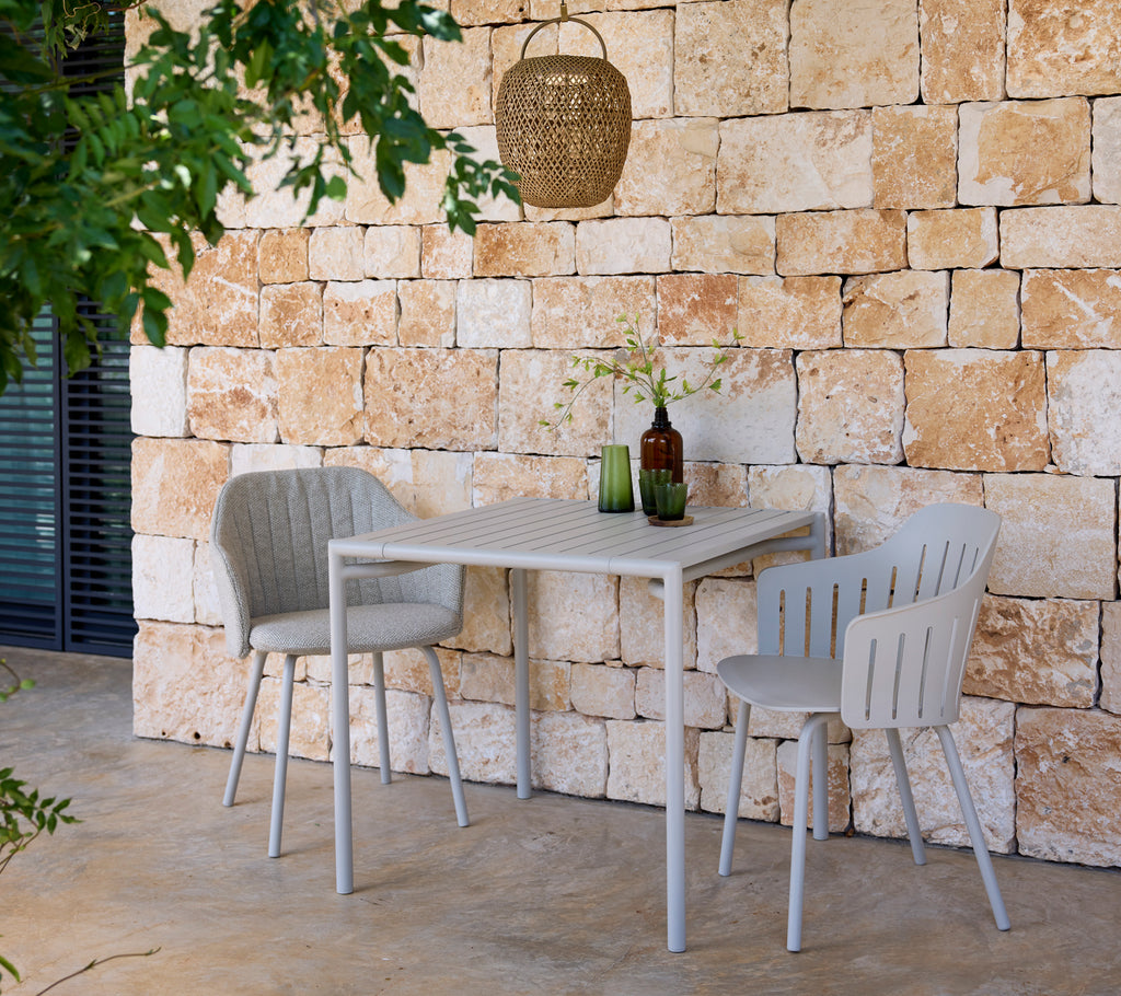 Mesa y sillas grises modernas con botellas verdes y marrones en un entorno al aire libre.