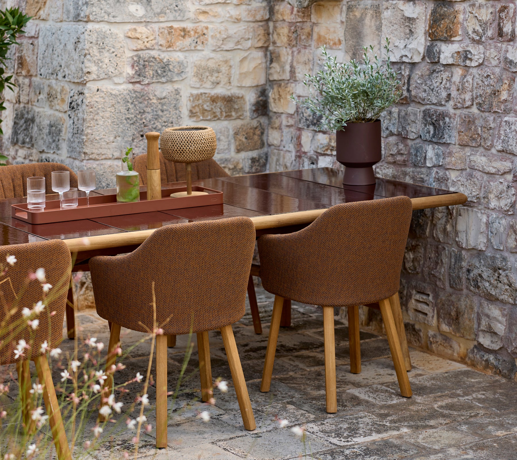 Sillas marrones alrededor de una mesa marrón con un jarrón decorativo en un entorno al aire libre.