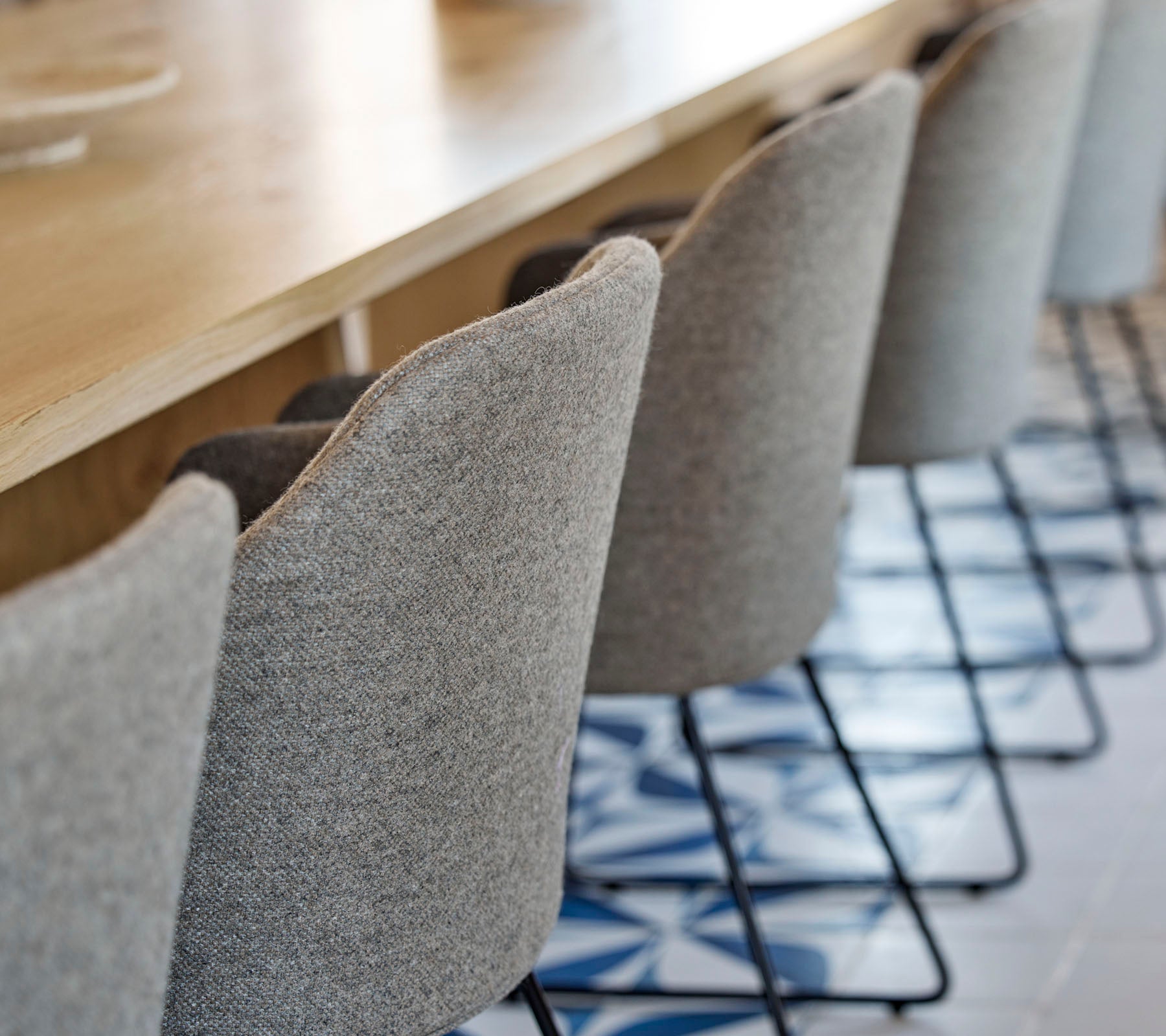 Una fila de sillas elegantes y tapizadas con patas de metal delgadas situadas alrededor de una mesa de madera, con un suelo de patrones debajo.