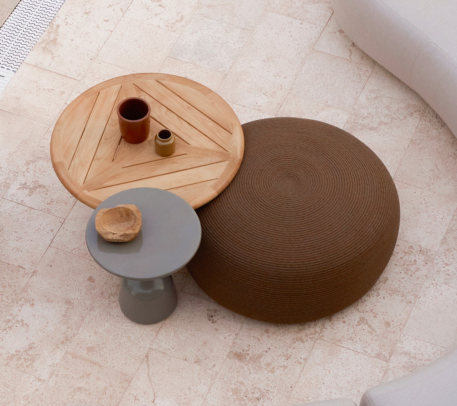 Un gran pouf circular en marrón al lado de una mesa de café de madera con un diseño geométrico, que presenta pequeños elementos decorativos en la parte superior.