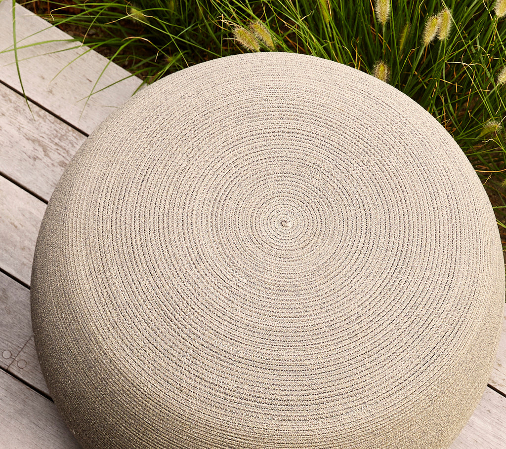 Puff redondo color taupe con una superficie texturizada que presenta patrones en espiral, ideal para asientos versátiles o decoración.