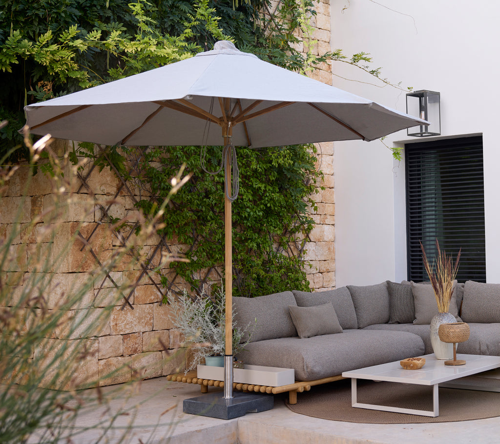 Zona de estar moderna con un sofá gris, mesa blanca y paraguas gris.