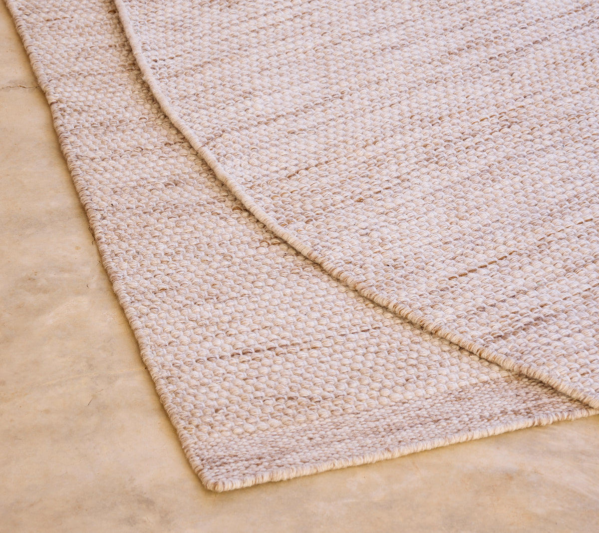Alfombra beige con un patrón texturizado sobre un suelo de color claro.