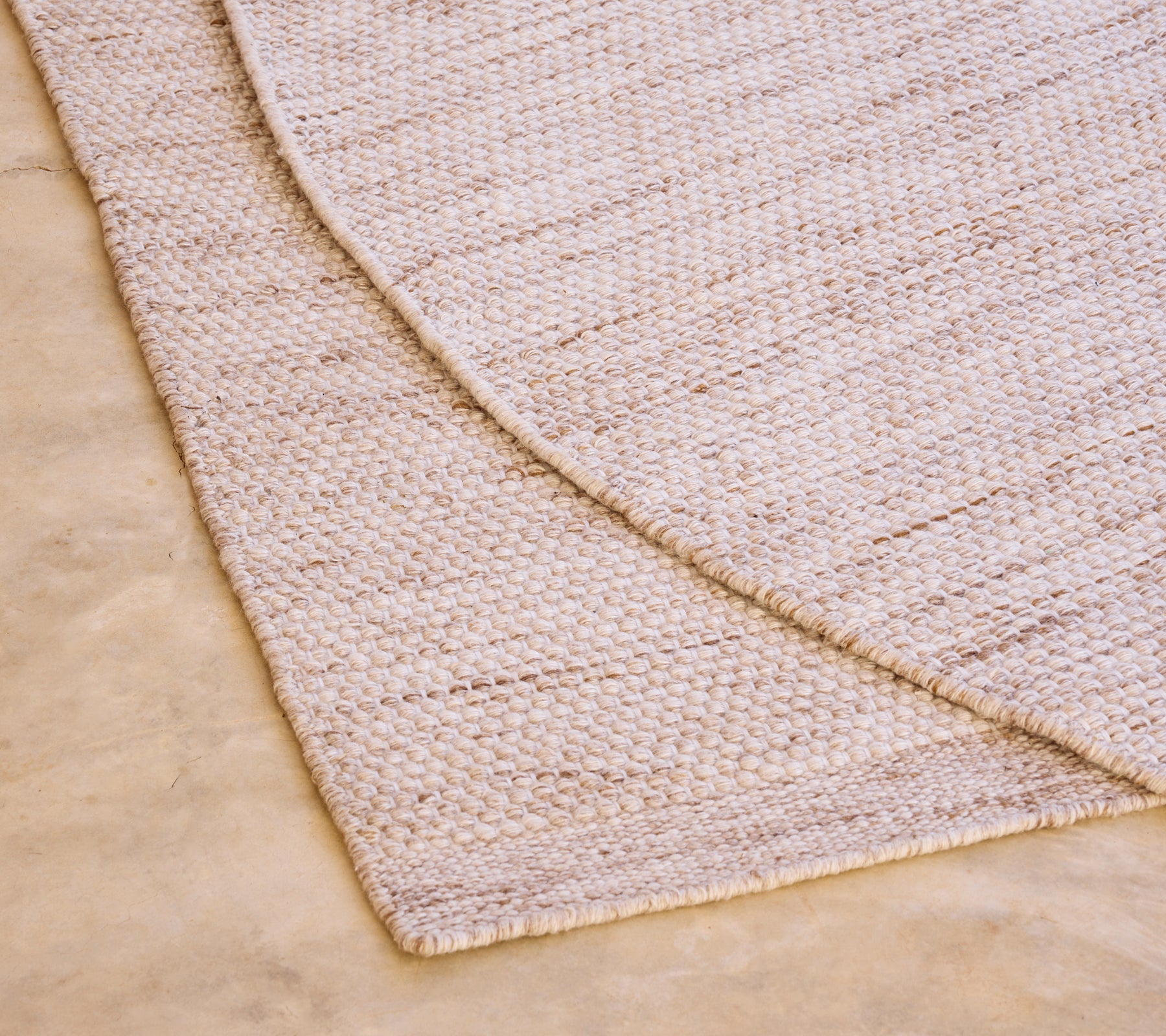 Alfombra beige con un patrón texturizado sobre un suelo de color claro.