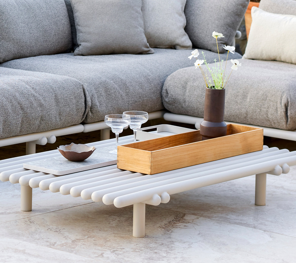 Una mesa de café elegante con una caja de almacenamiento de teca, que presenta un diseño minimalista y elementos decorativos como copas y un pequeño jarrón.