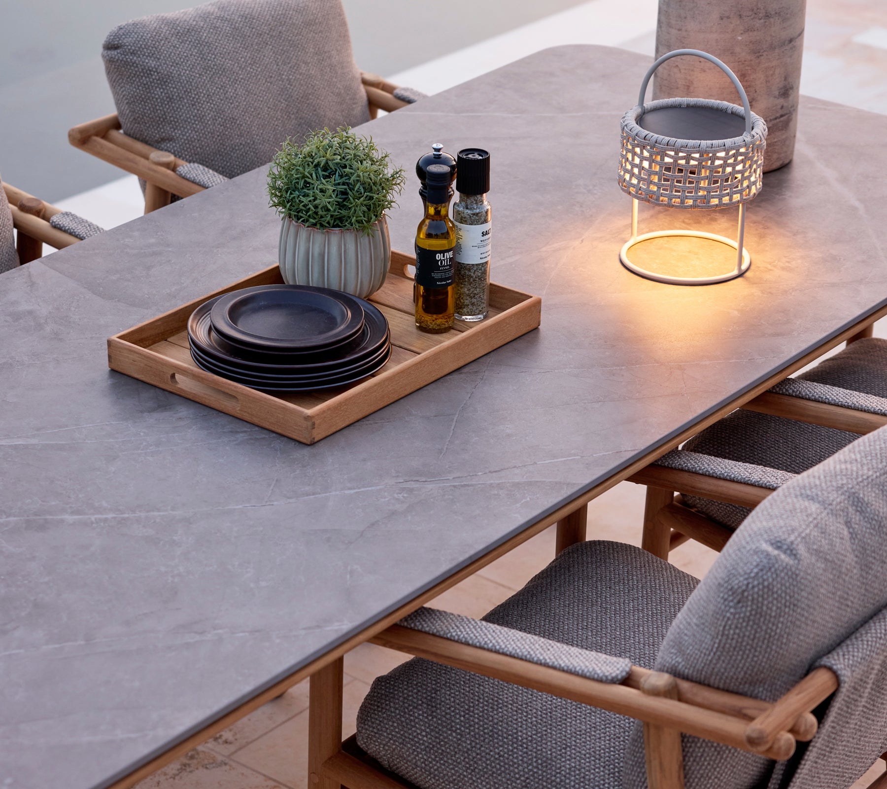 Mesa de comedor moderna con superficie gris, sillas marrones, platos negros y una linterna decorativa.
