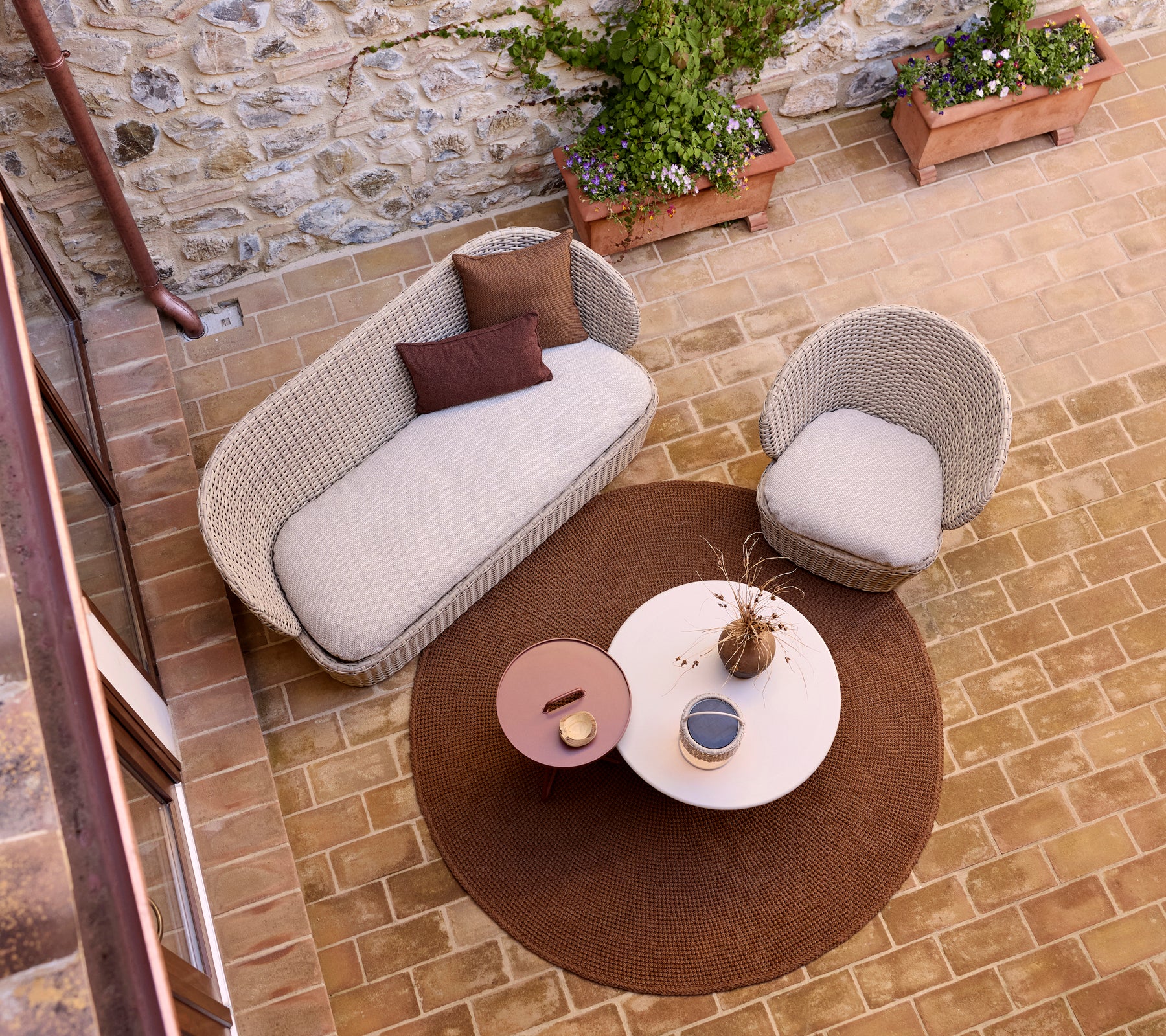 Área de lounge acogedora con una alfombra de punto, mesa de café de vidrio y una lámpara de ilusión, acentuada con plantas en macetas.