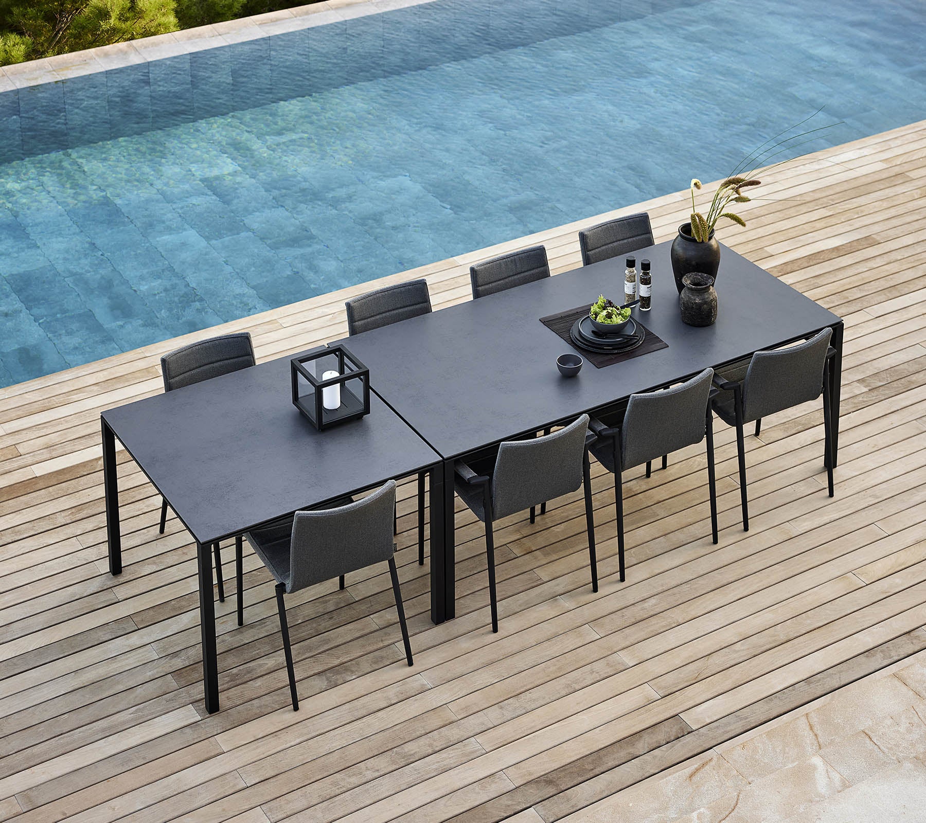 Una elegante disposición de comedor con una mesa pura y sillas modernas, adornada con plantas decorativas y accesorios, junto a una tranquila piscina.