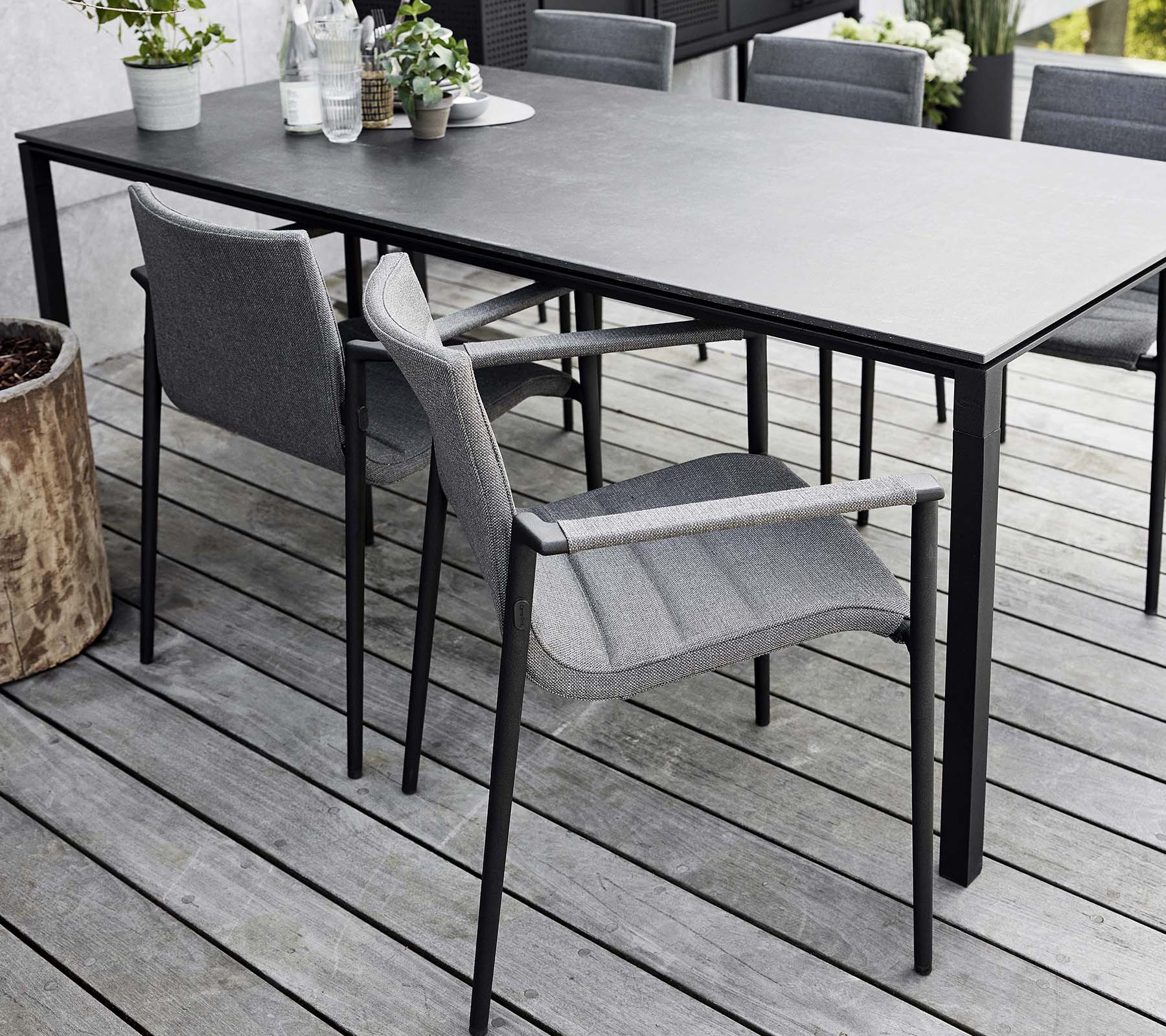 Montaje de comedor elegante con una mesa estilizada y modernas sillas grises, rodeado de elementos naturales y vegetación.