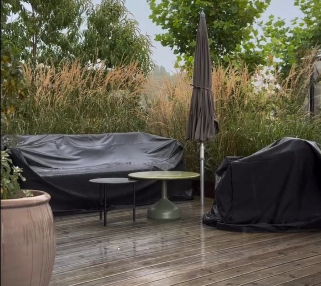 Espacio exterior con sofá negro, mesa verde y silla negra rodeada de vegetación.