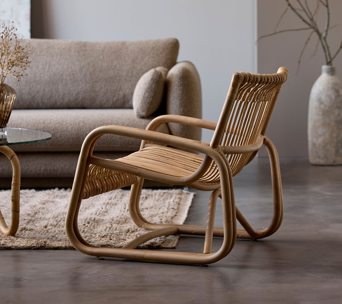 Silla de ratán al lado de un sofá beige y una mesa de cristal en un ambiente moderno de salón.