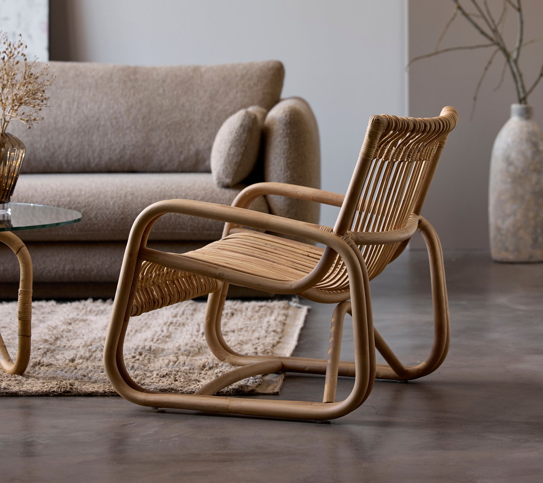Silla de ratán al lado de un sofá beige y una mesa de cristal en un ambiente moderno de salón.
