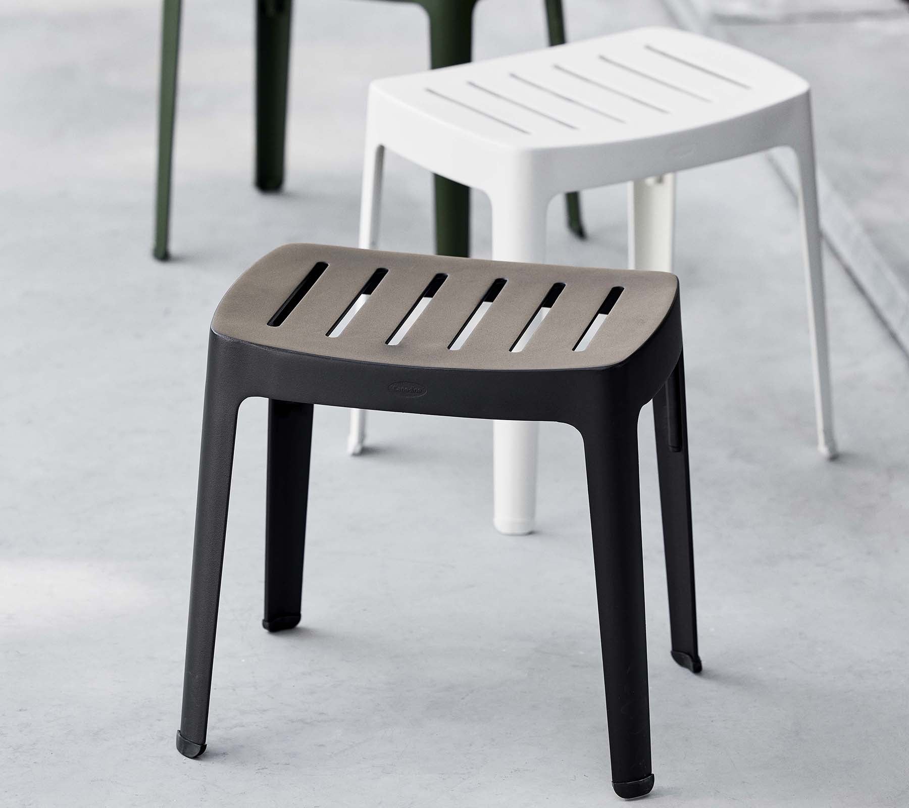 Taburete elegante en negro con tapa de listones, que presenta un diseño moderno; complementado por un taburete blanco en el fondo.