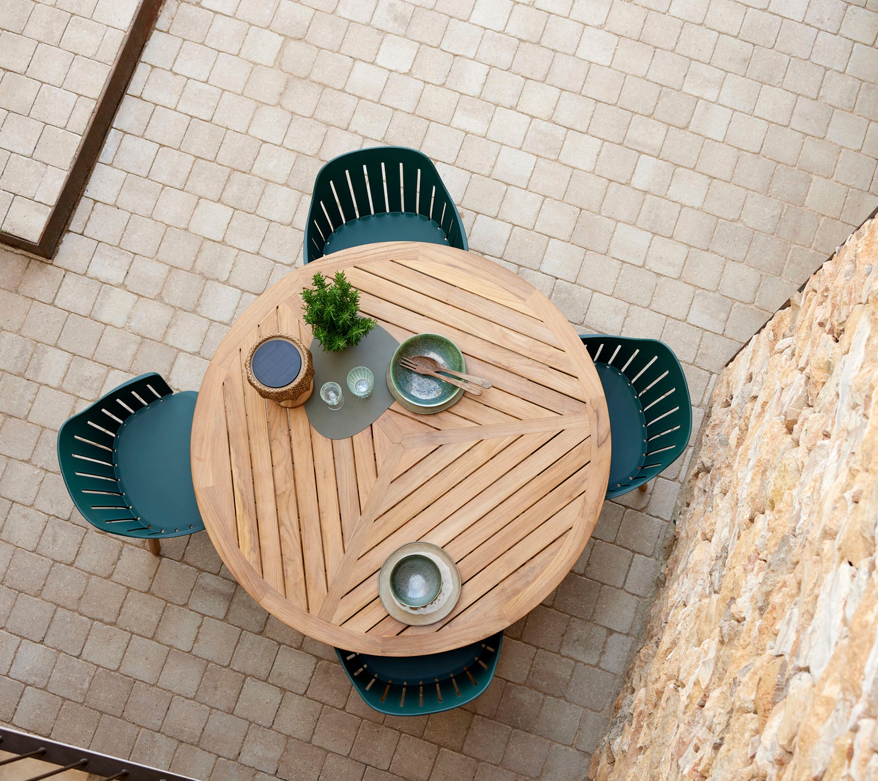 Una mesa redonda de madera con un patrón en chevrón, rodeada por cuatro sillas verdes, y adornada con platos decorativos y una planta pequeña.