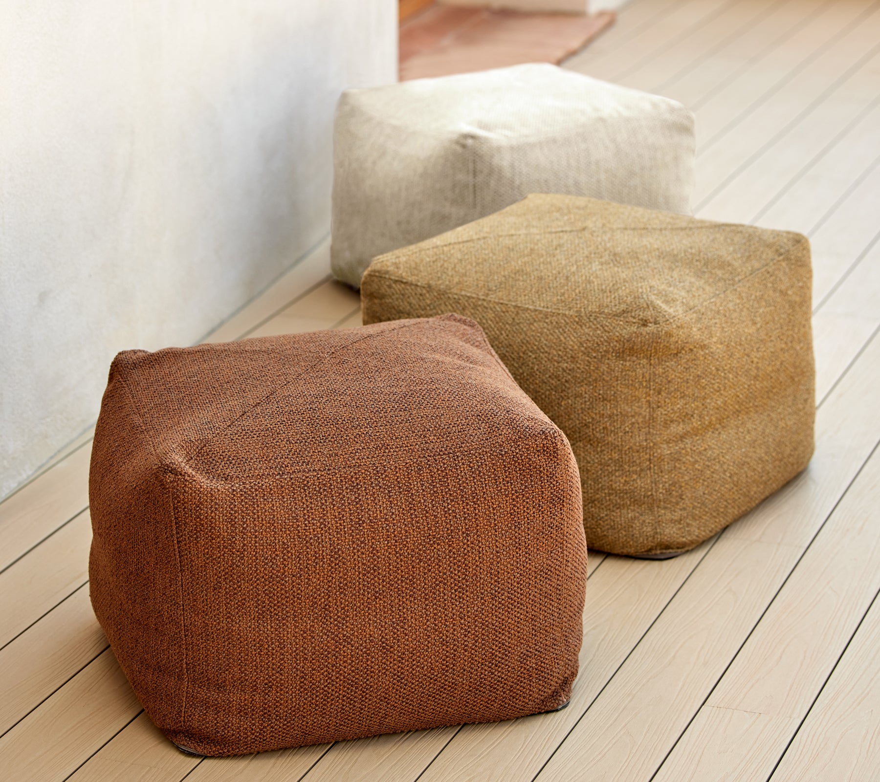 Tres puff texturizados en tonos terrenales de marrón, beige y canela, exhibidos en una superficie de madera. Ideal para asientos y decoración versátiles.