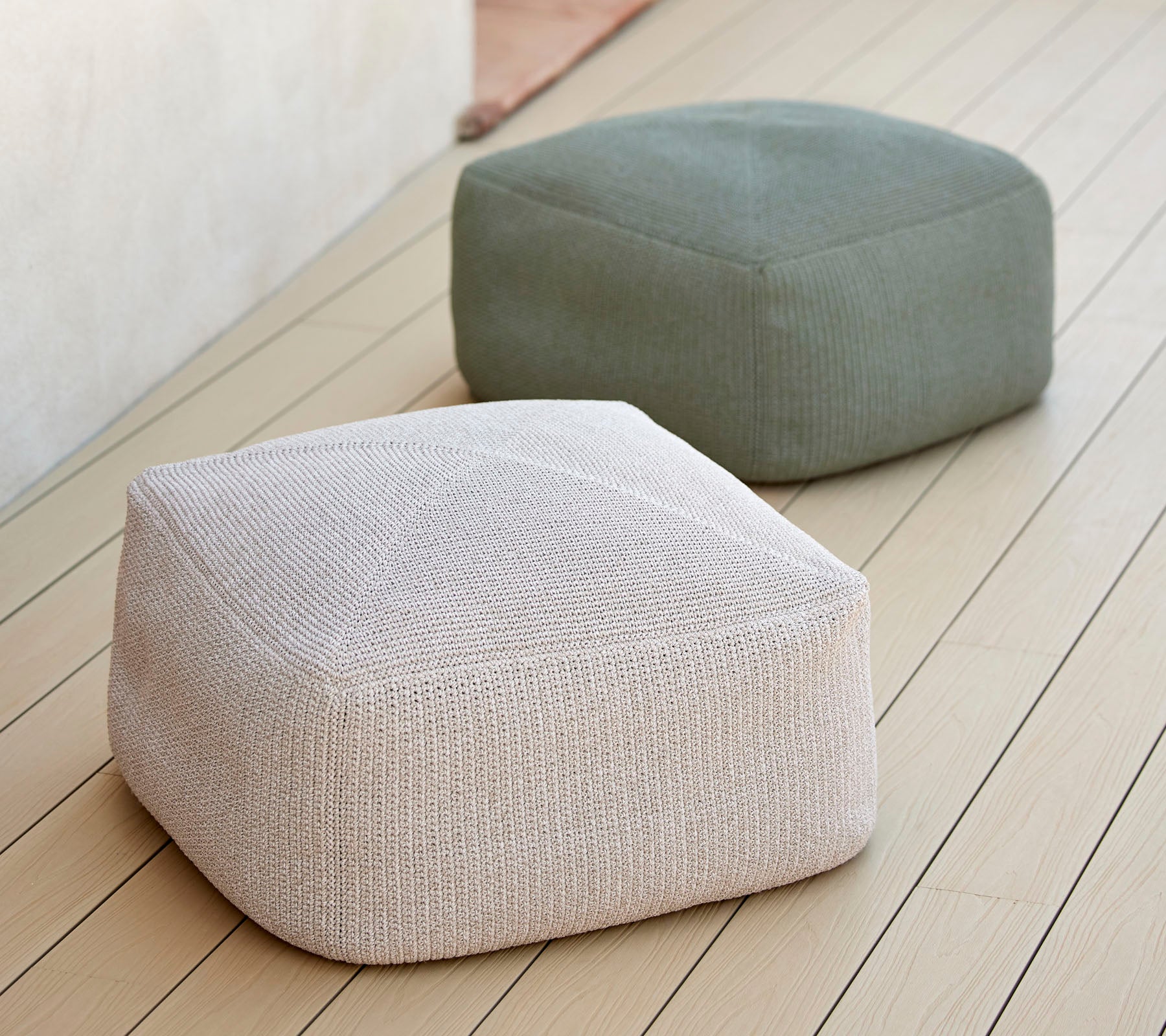 Dos poufs elegantes y texturizados en tonos neutros, uno blanco y otro verde, dispuestos sobre una superficie suave, ideales para asientos versátiles.