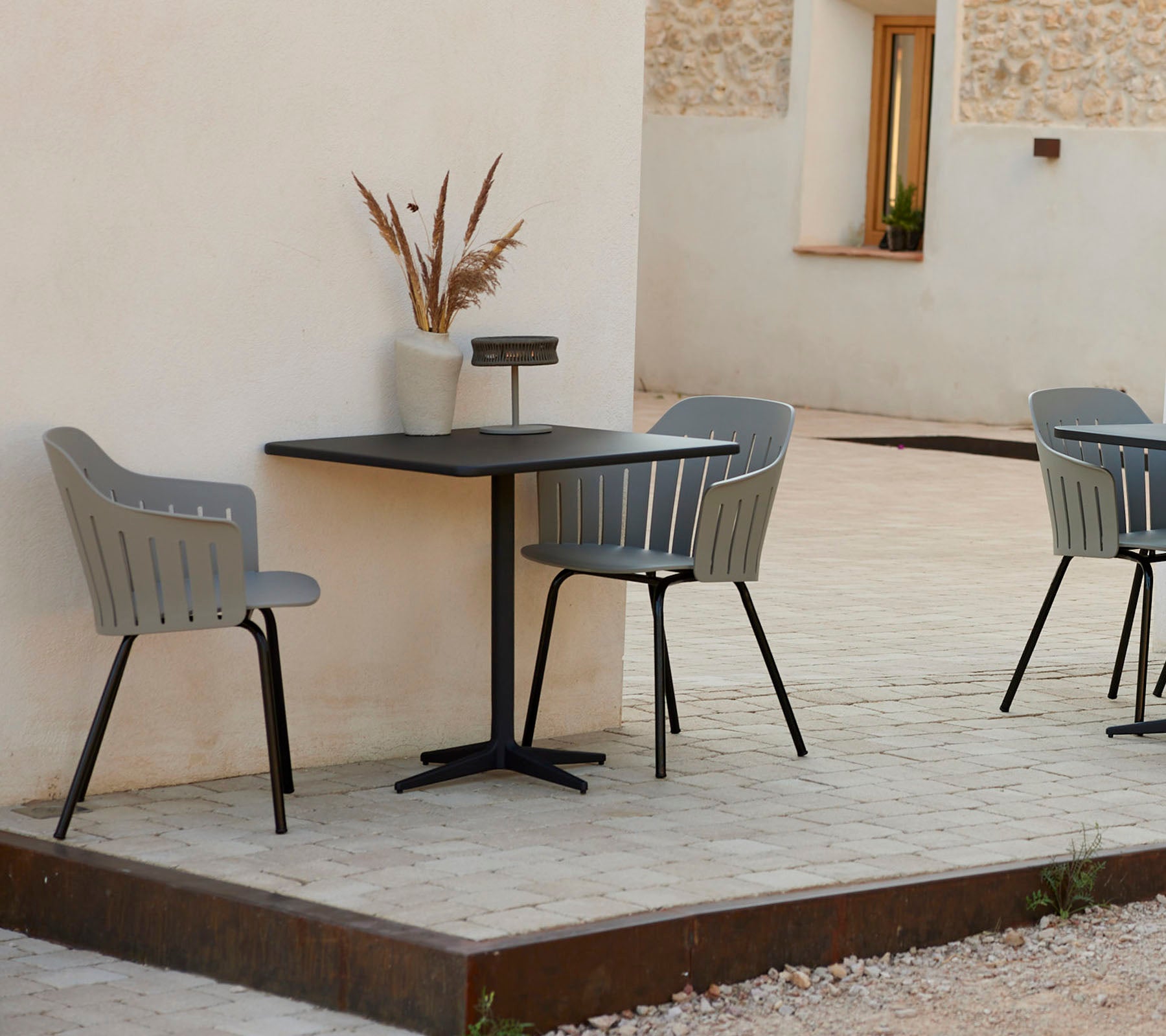 Una mesa de café moderna con dos sillas grises elegantes, acompañada de un jarrón decorativo, situada contra un fondo sencillo.
