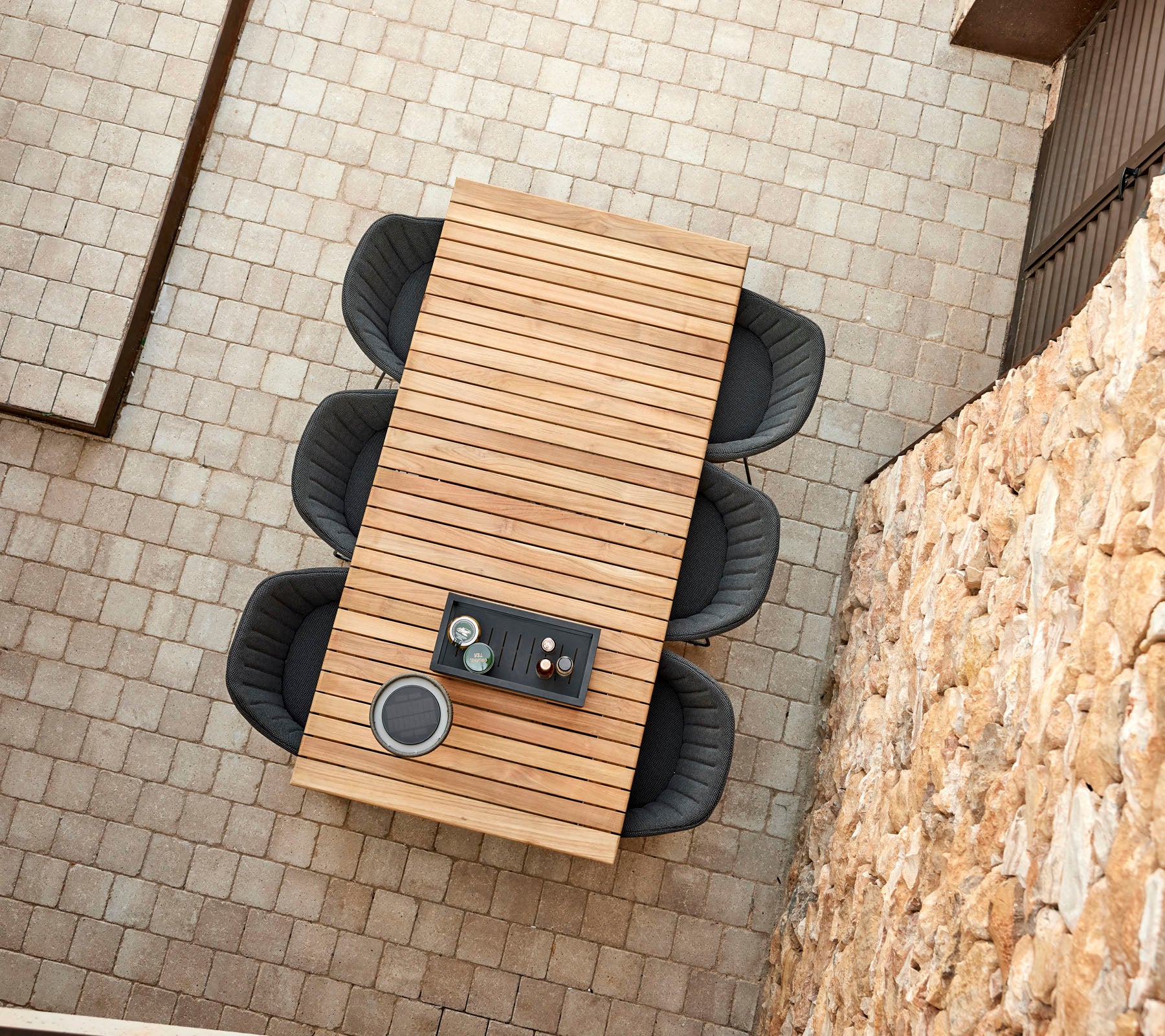 Una mesa de madera moderna con cuatro sillas negras elegantes, con un arreglo central de bebidas y aperitivos.