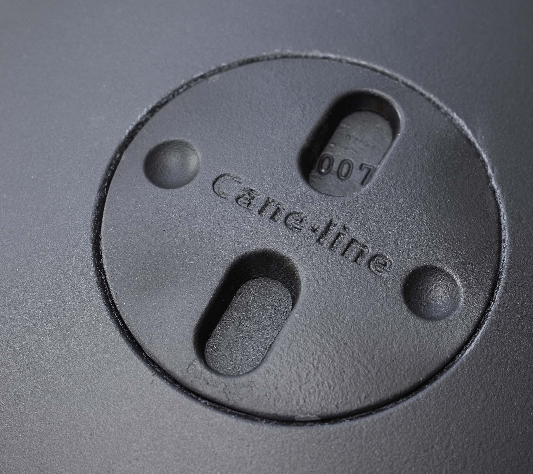 Acercamiento de una característica circular con el logo "Cane-line" grabado y dos ranuras, parte de un diseño de fogón.