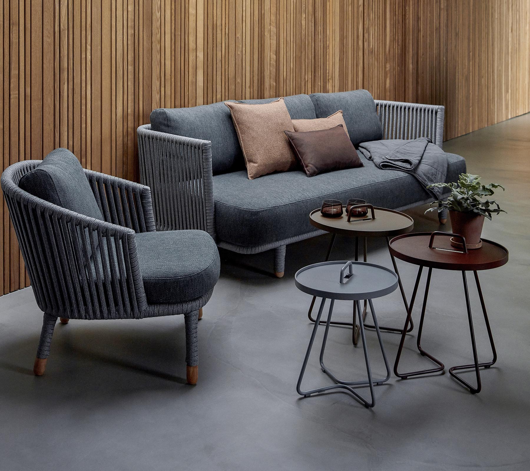 Arreglo de asientos elegante con un sofá gris con cojines y dos sillas de acento, junto con tres mesas modernas y una planta en maceta.
