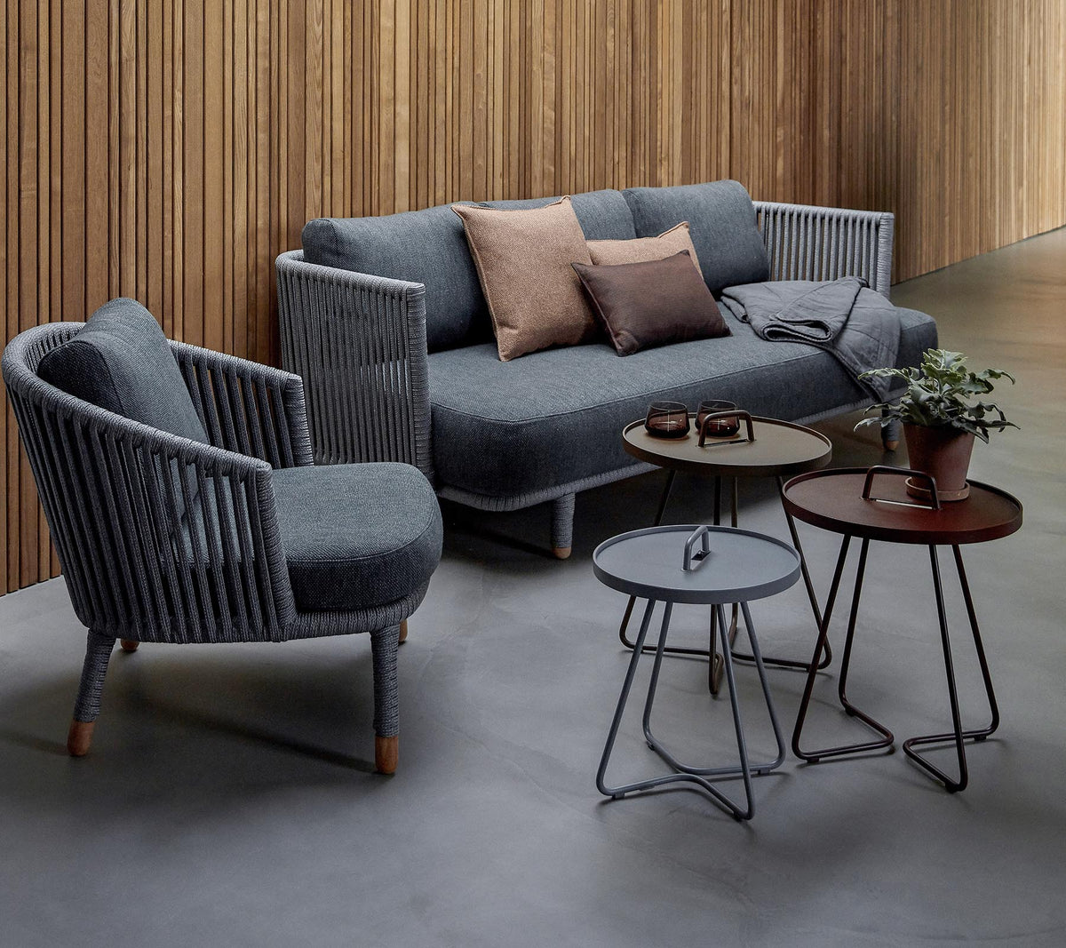 Arreglo de asientos elegante con un sofá gris con cojines y dos sillas de acento, junto con tres mesas modernas y una planta en maceta.
