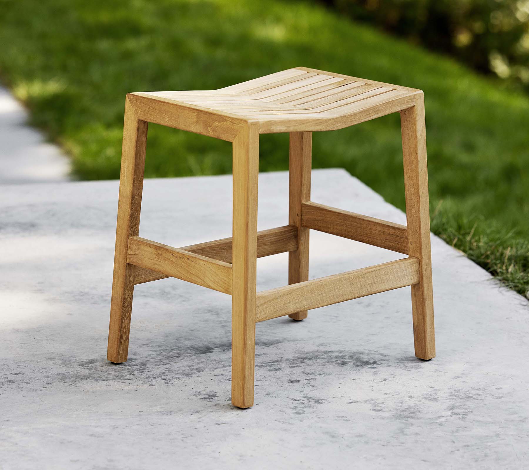 Un taburete de madera plegable con un asiento ranurado y patas robustas, diseñado para uso versátil como asiento o decorativo.