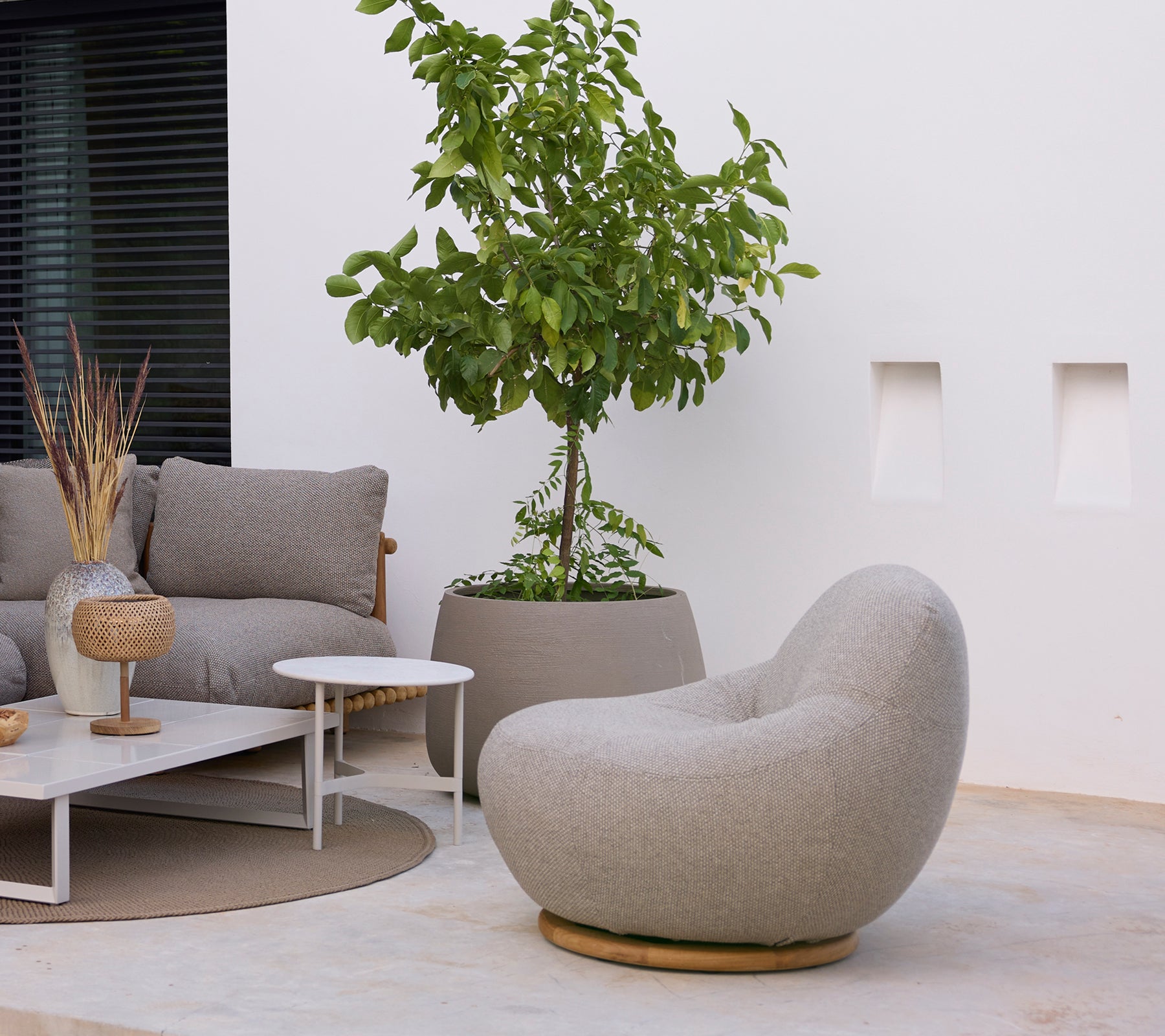 Área de lounge moderna con una silla gris, un sofá, una mesa de café blanca y una planta verde.