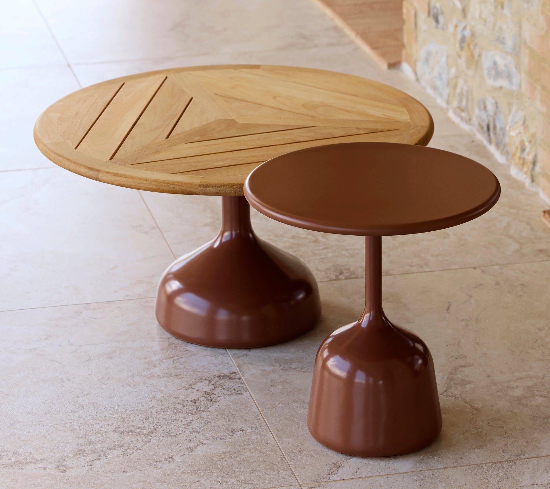 Dos mesas de café, una con una parte superior de madera y diseño geométrico, la otra con un acabado suave de color rojo desierto, compartiendo una estética moderna.