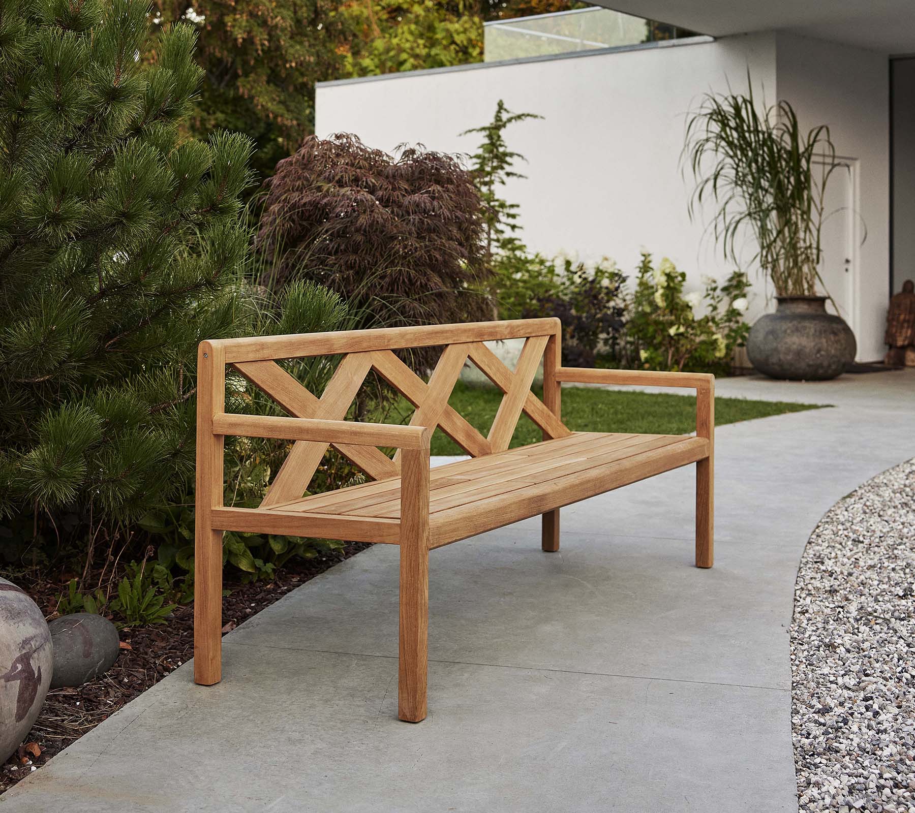 Un elegante banco de madera con un respaldo decorativo, rodeado de vegetación y elementos decorativos, perfecto para relajarse al aire libre.
