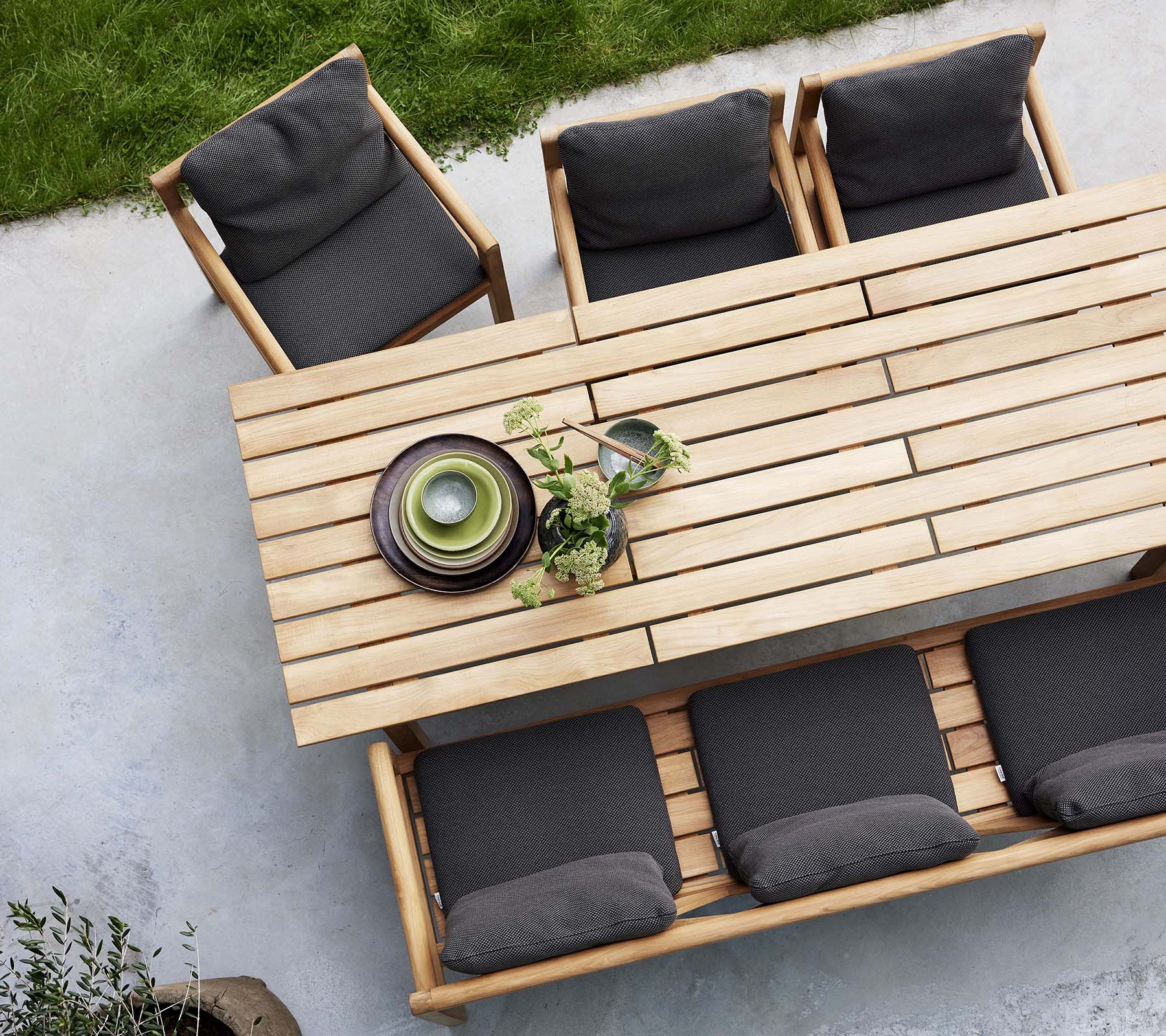 Un juego de comedor de madera que incluye una mesa, un banco y sillas con cojines oscuros, acentuado por platos decorativos y vegetación.