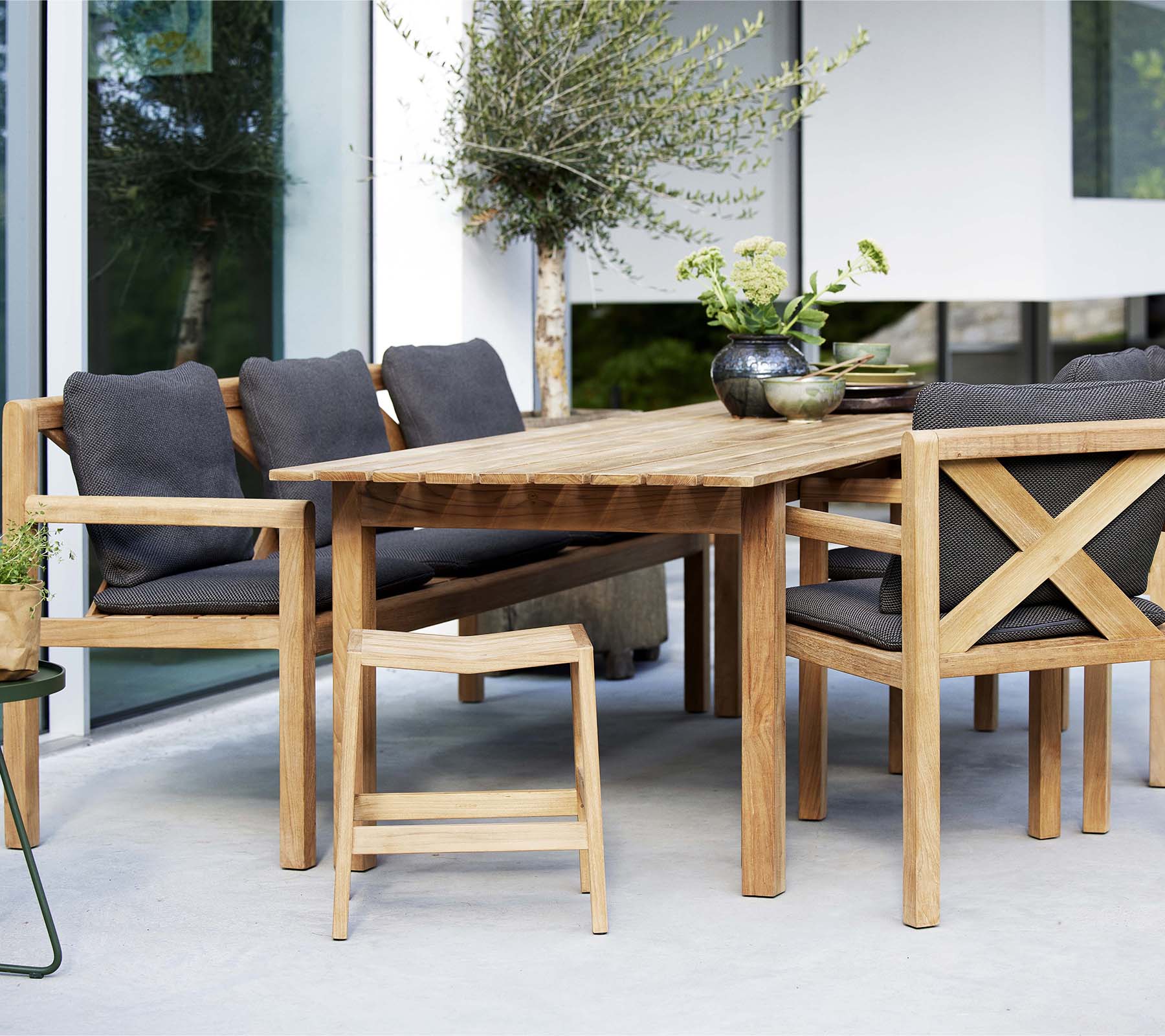 Una mesa de madera rodeada de sillas elegantes y un banco, con cojines suaves y plantas decorativas para una zona de estar acogedora.