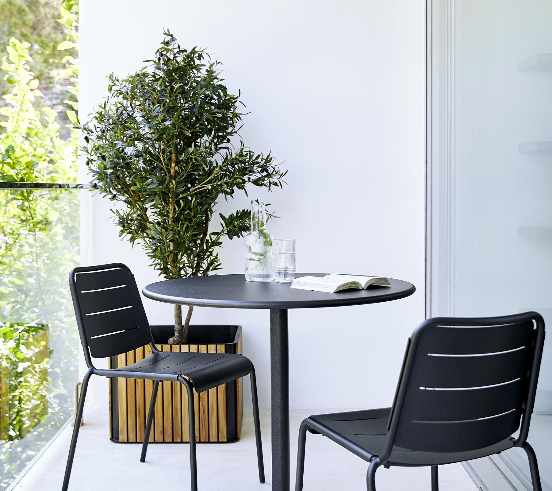 Una configuración moderna de comedor con una mesa redonda, dos sillas negras y una planta en maceta, creando una atmósfera elegante y acogedora.