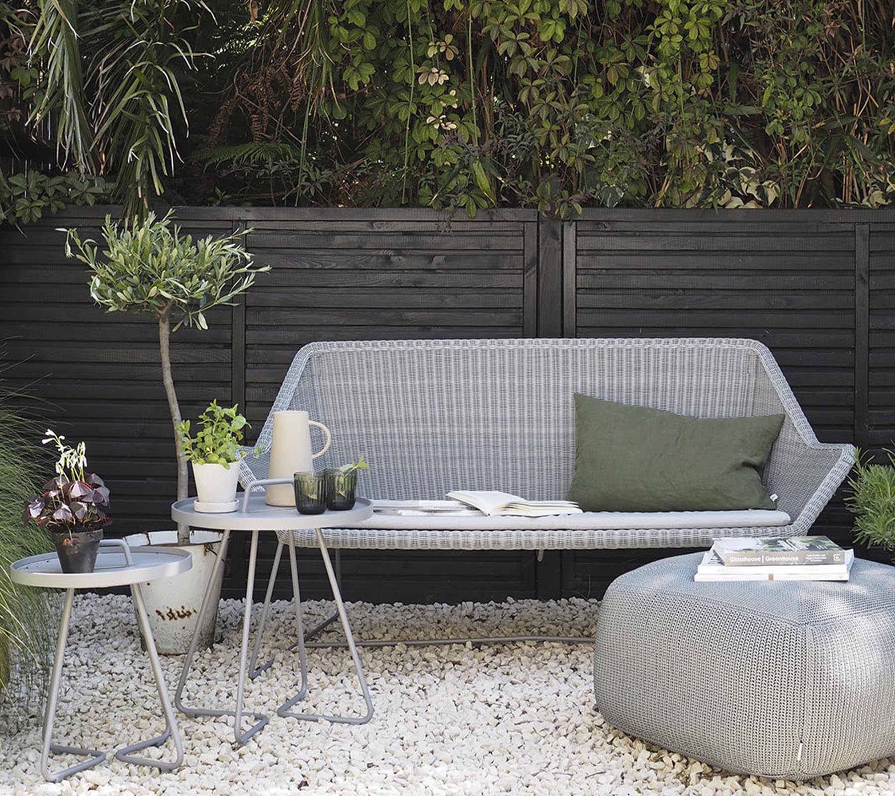 Arreglo de muebles de exterior minimalista que presenta un sofá elegante, mesas auxiliares y plantas decorativas en una superficie de grava.