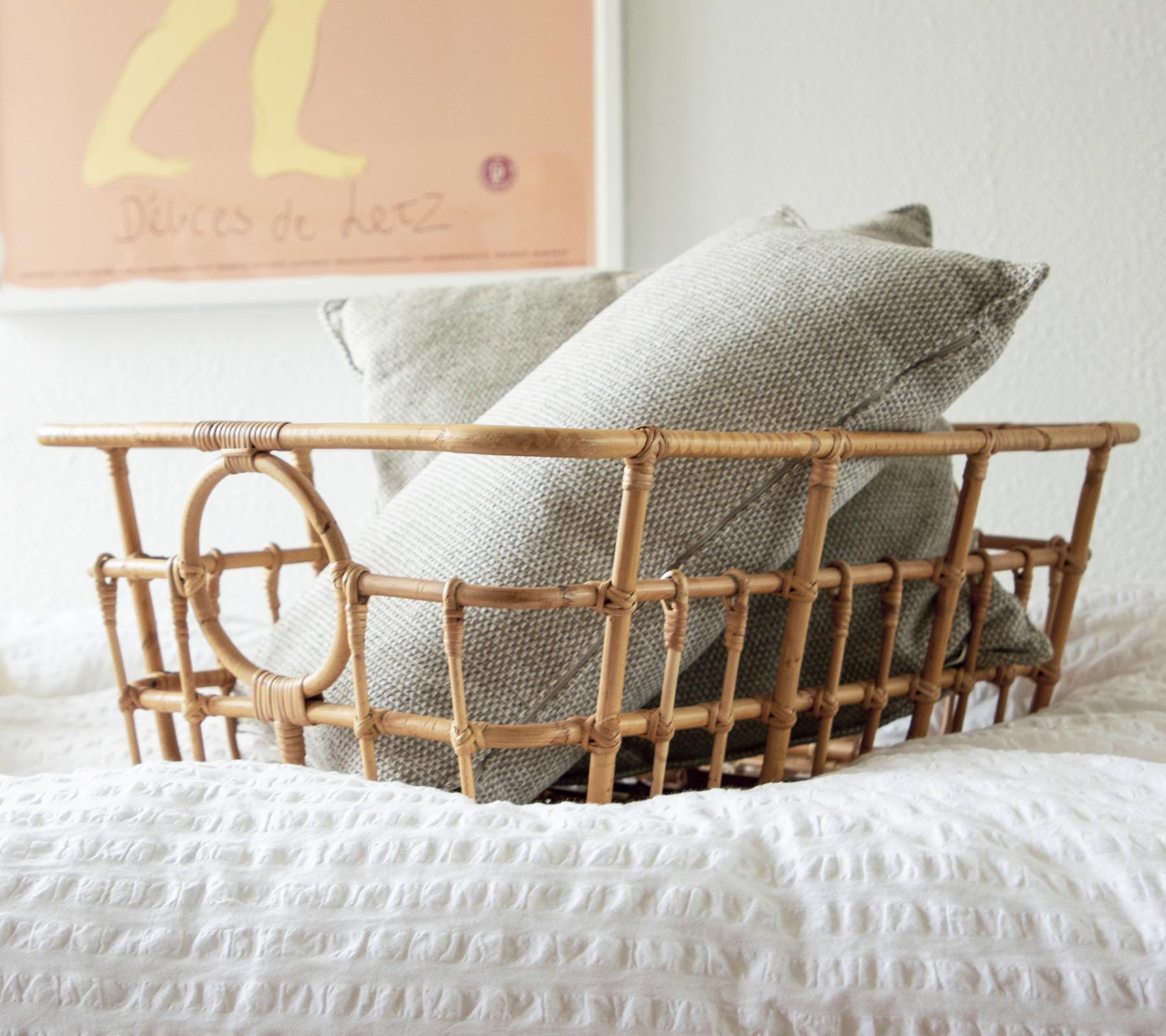 Cesta de ratán con cojines grises y blancos en un ambiente acogedor de dormitorio.