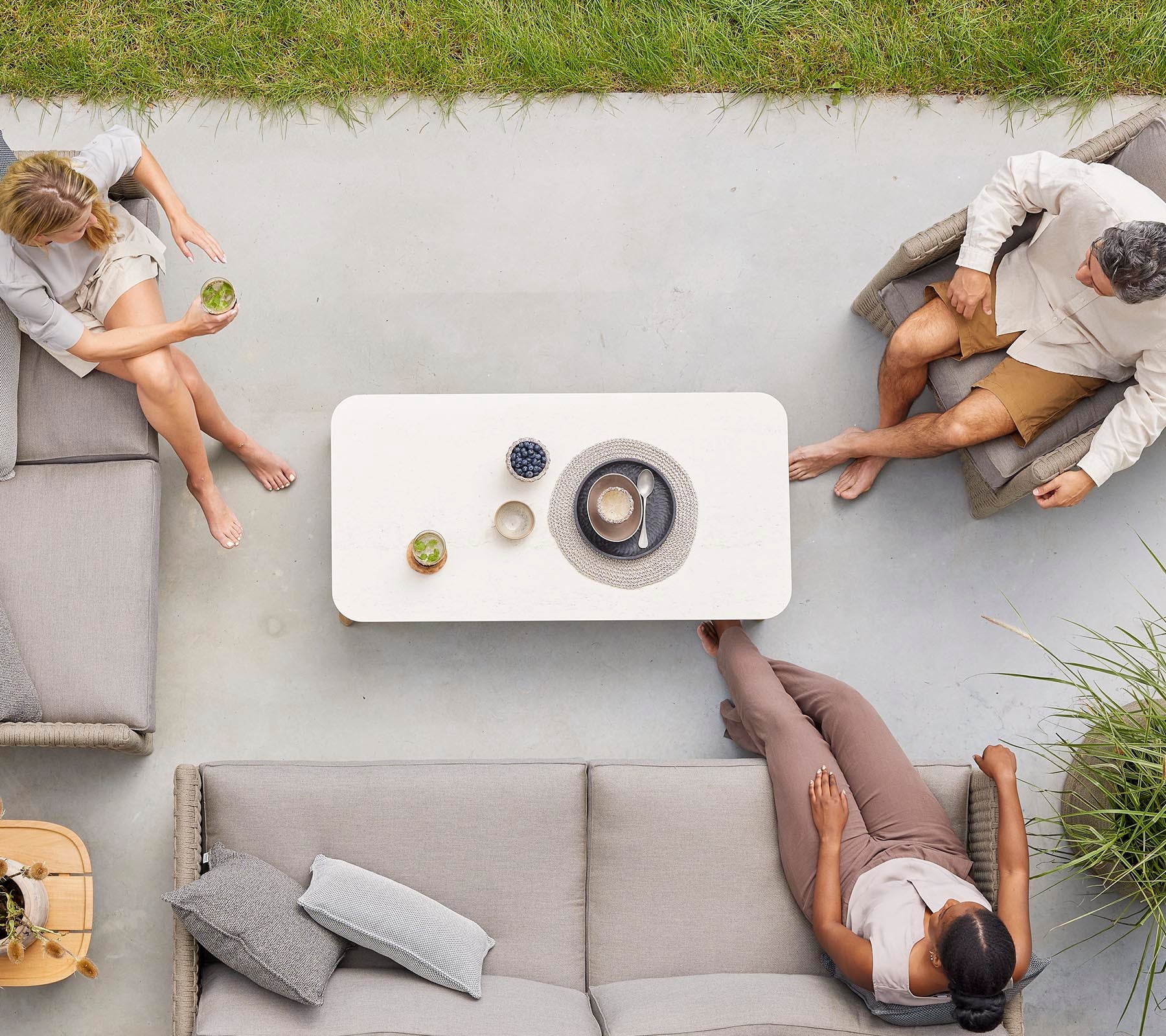 Vista aérea de tres personas sentadas alrededor de una mesa de café con bebidas, disfrutando de una reunión relajada en un entorno informal.