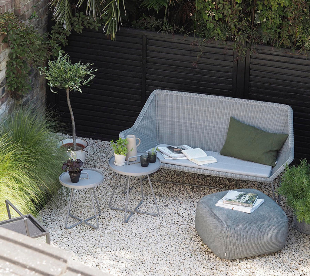 Sofá gris moderno con cojín verde y mesa lateral gris en un área de salón minimalista.