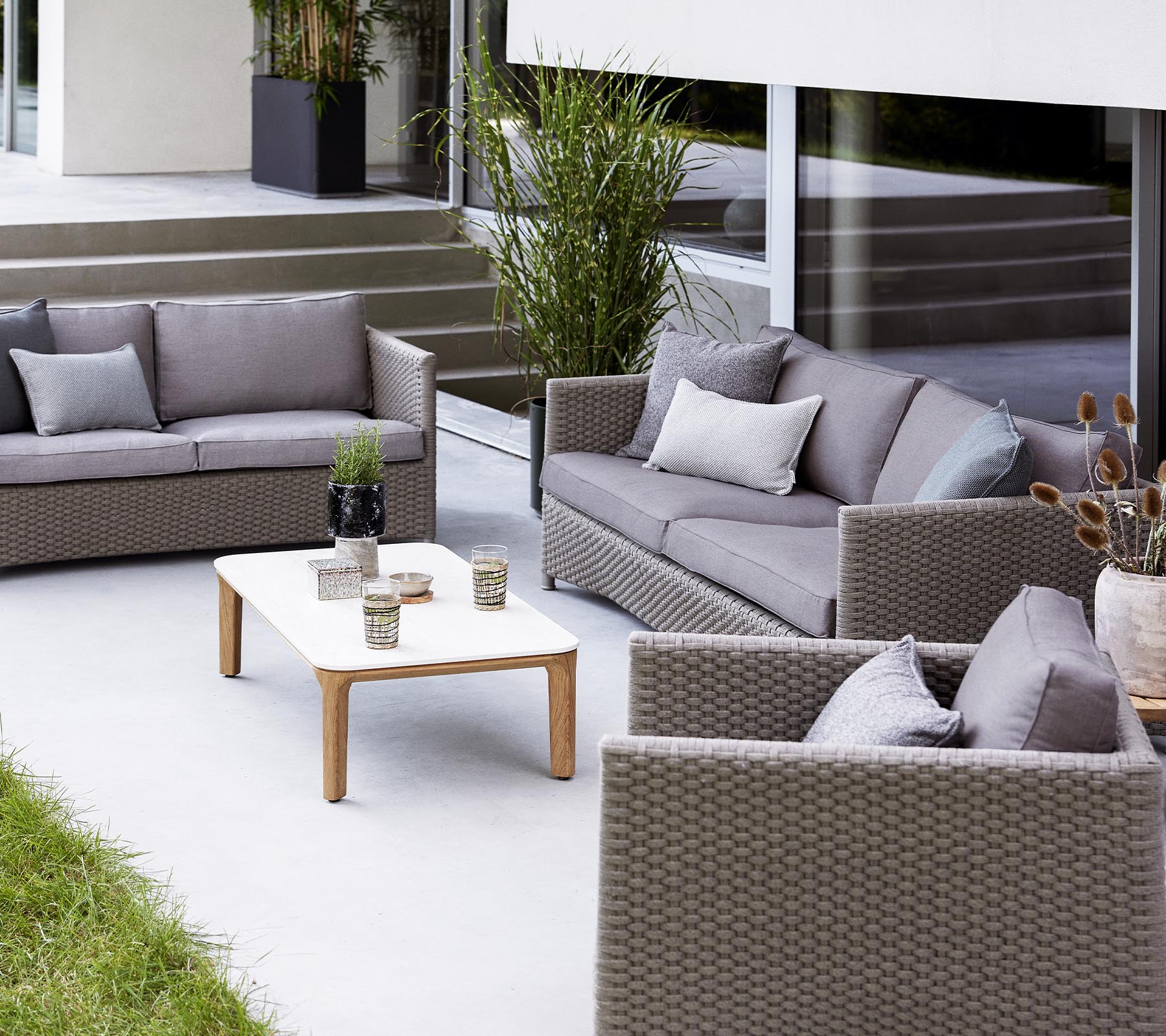 Conjunto contemporáneo de asientos al aire libre que incluye un sofá de 2 plazas, un sofá de 3 plazas, sillas de lounge y una mesa de café con elementos decorativos.