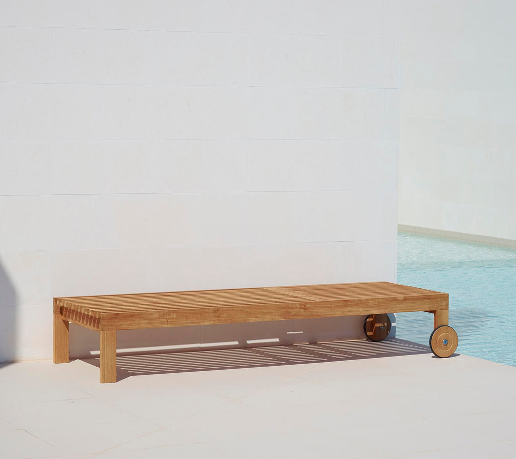 Tumbona de madera con un diseño minimalista, que cuenta con una superficie lisa y una rueda para facilitar la movilidad. Ideal para relajarse junto a la piscina.