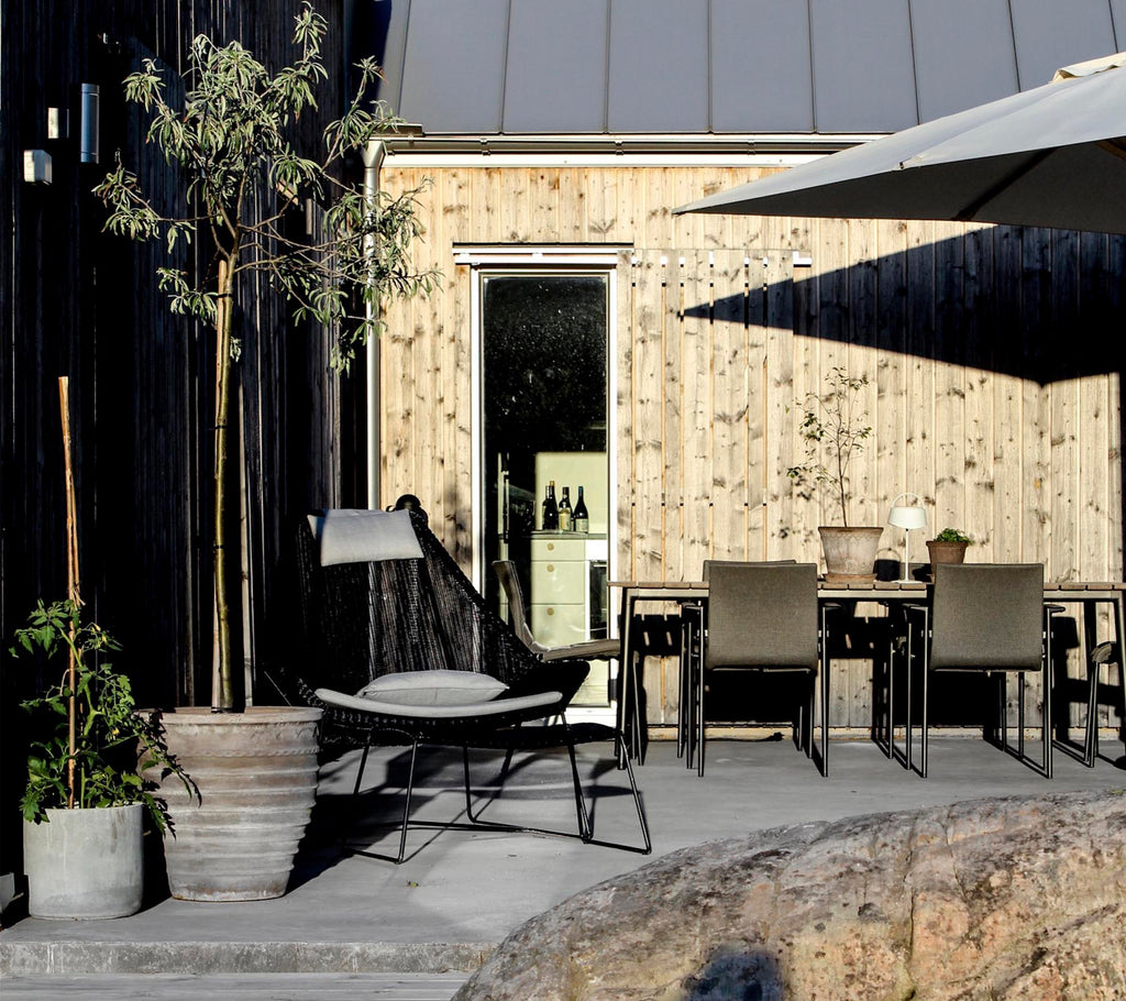 Área de salón al aire libre con una silla negra, una mesa gris y una planta en maceta.