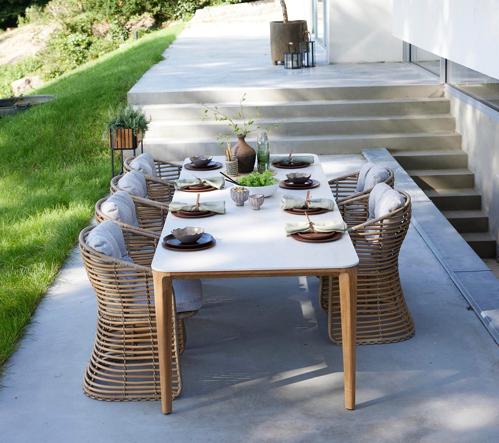 Un elegante conjunto de mesa de comedor al aire libre con sillas de mimbre redondas, dispuestas elegantemente con platos y un centro de mesa de vegetación.