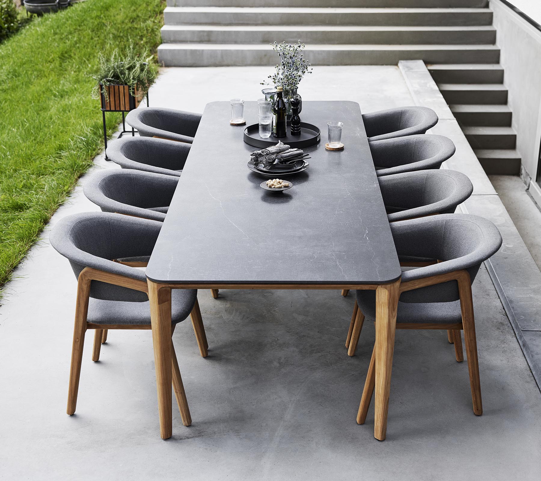 Configuración de comedor elegante con una mesa larga rodeada de modernas sillas tapizadas, adornada con objetos decorativos y vegetación.