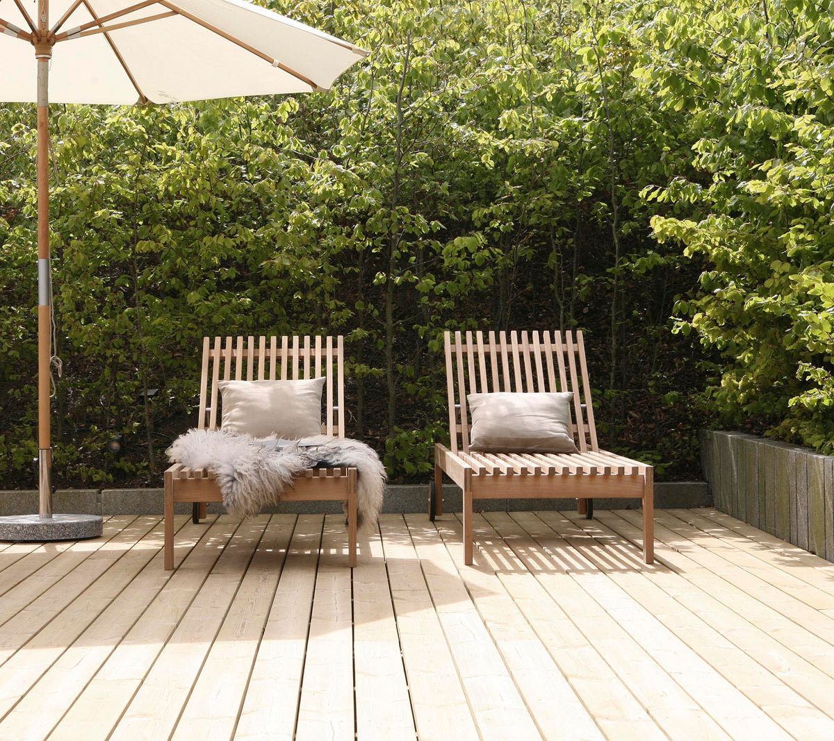 Dos sillas de estilo de madera con cojines, situadas en una terraza de madera, rodeadas de vegetación y con una gran sombrilla cerca.