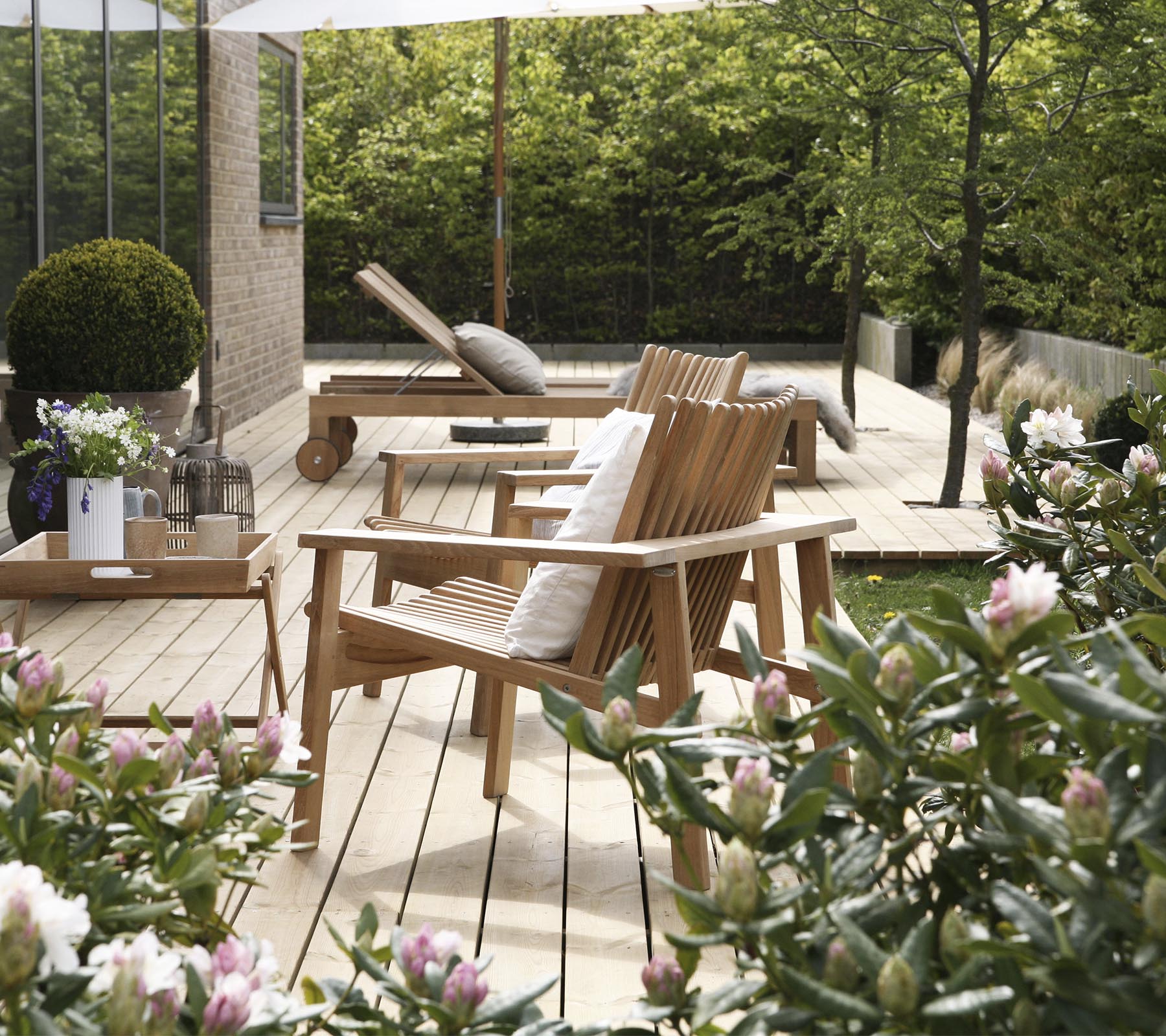 Sillas de madera y una mesa están rodeadas de vegetación y flores, creando un área de asientos al aire libre serena y acogedora.